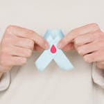 Close-up of a person holding a blue awareness ribbon featuring a red blood drop symbol.